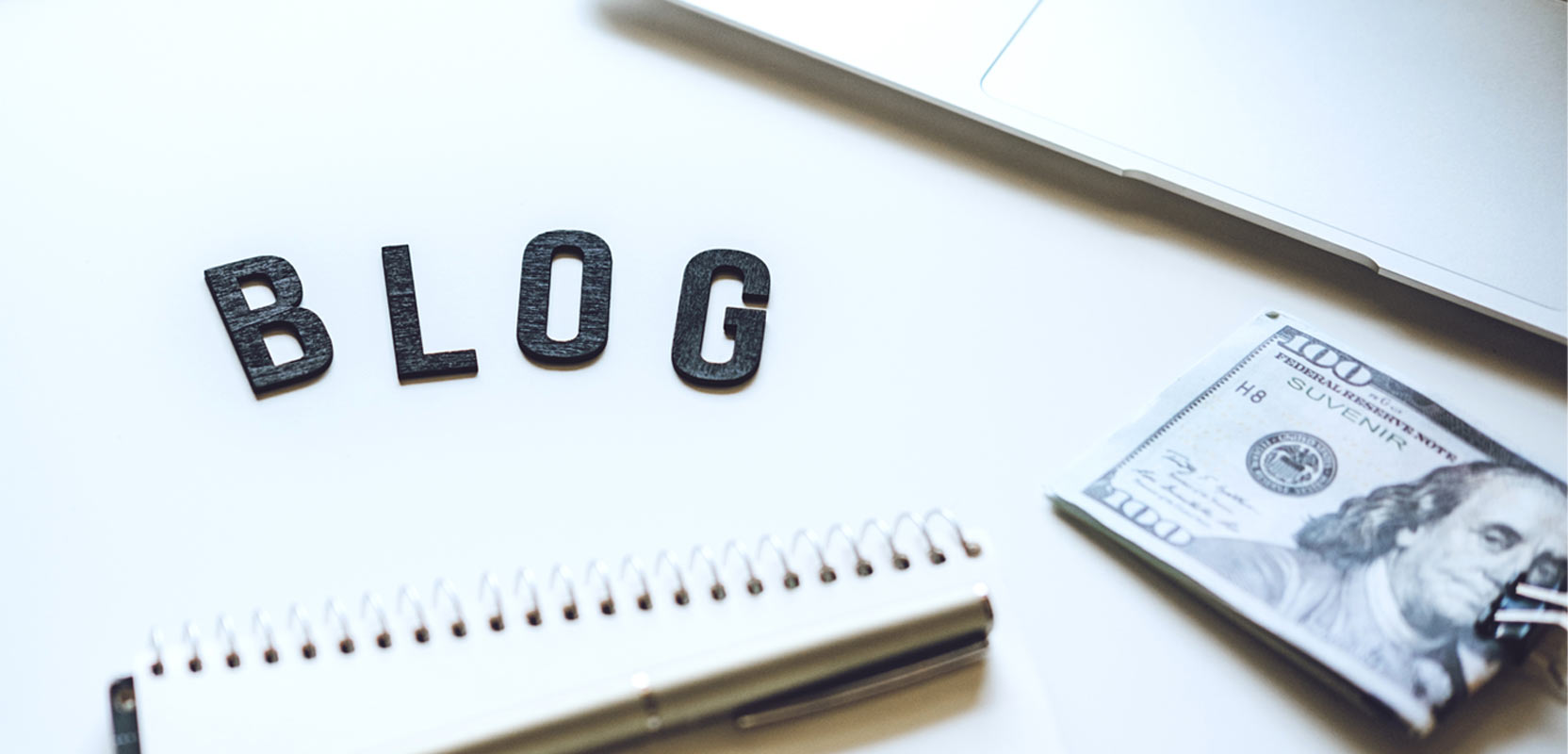 Magnetic letters spelling out BLOG next to a notebook and a hundred-dollar bill