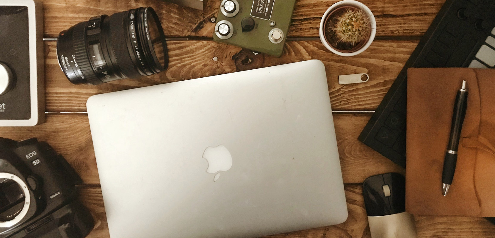 Desk with camera lenses, a notebook, a laptop, and other equipment for a photography side hustle