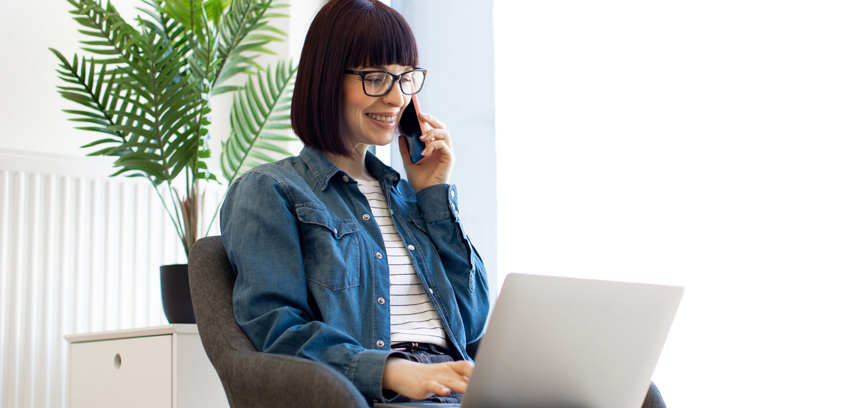 Freelance writer sitting at a laptop and talking on the phone while pitching a review to a magazine 
