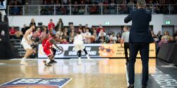 Professional basketball coach at an indoor basketball court supervising players in a game
