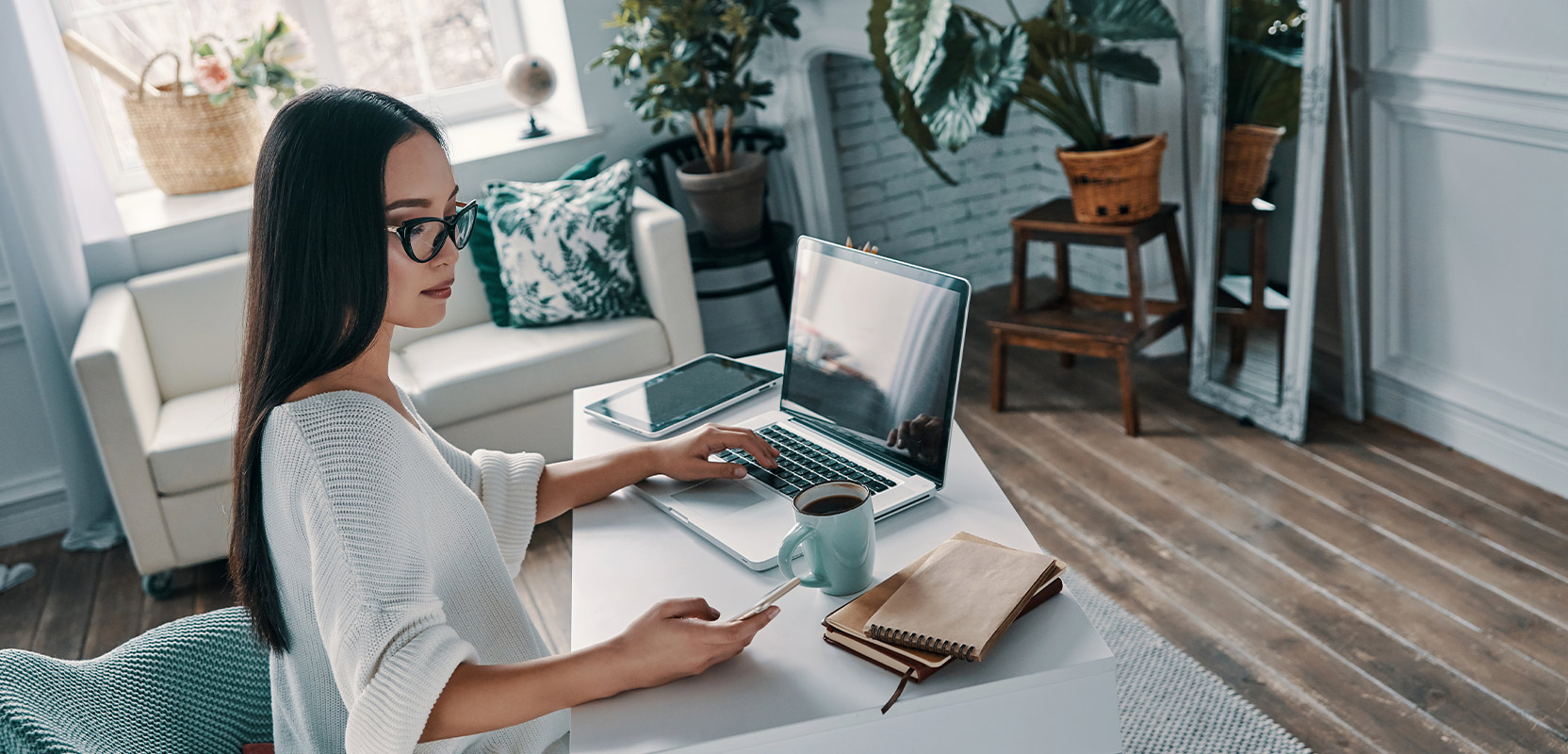 Online service provider sitting in her home office with her phone, tablet, computer, and a cup of coffee