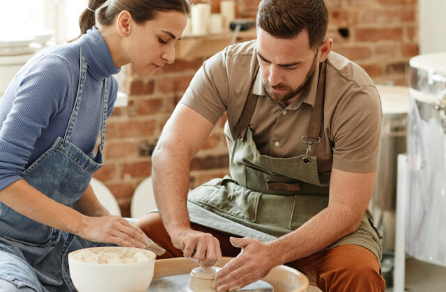 Couple in aprons at a pottery wheel, working together to create handmade artisan clay products