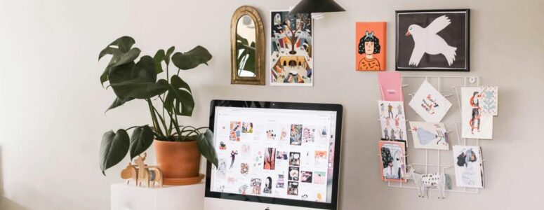 Remote work station for selling handmade items from home, featuring a desk, computer, and handmade cards pinned to the wall