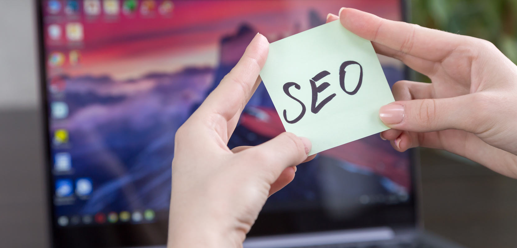Woman about to place a sticky note reading SEO on a laptop