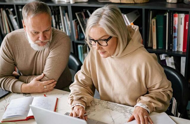 Two 50+ year olds working on a laptop for their side hustle together.
