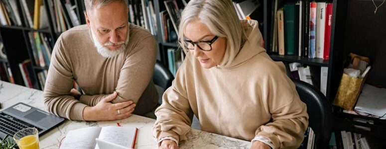 Two 50+ year olds working on a laptop for their side hustle together.