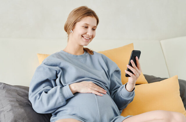 Pregnant mom sitting in bed working on a side hustle on her phone.