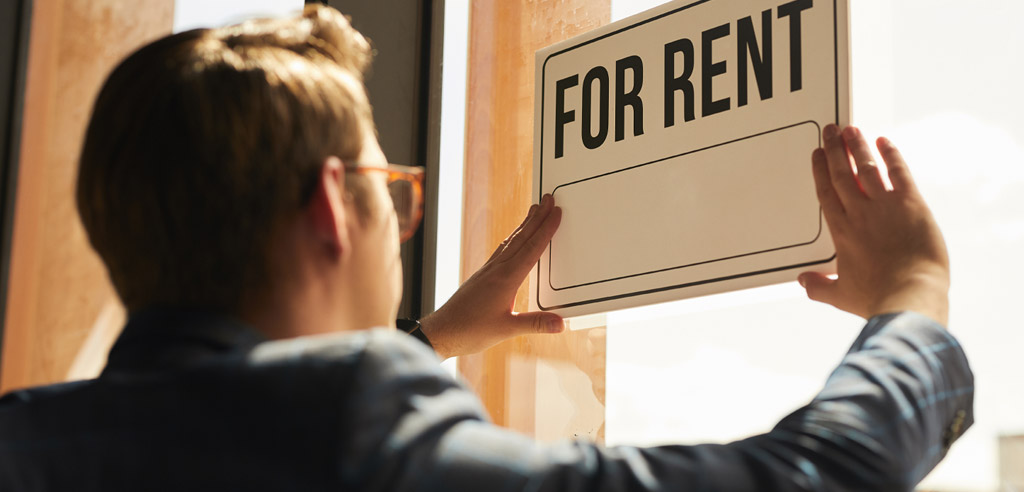 Person putting up a sign in a window that says "For Rent"