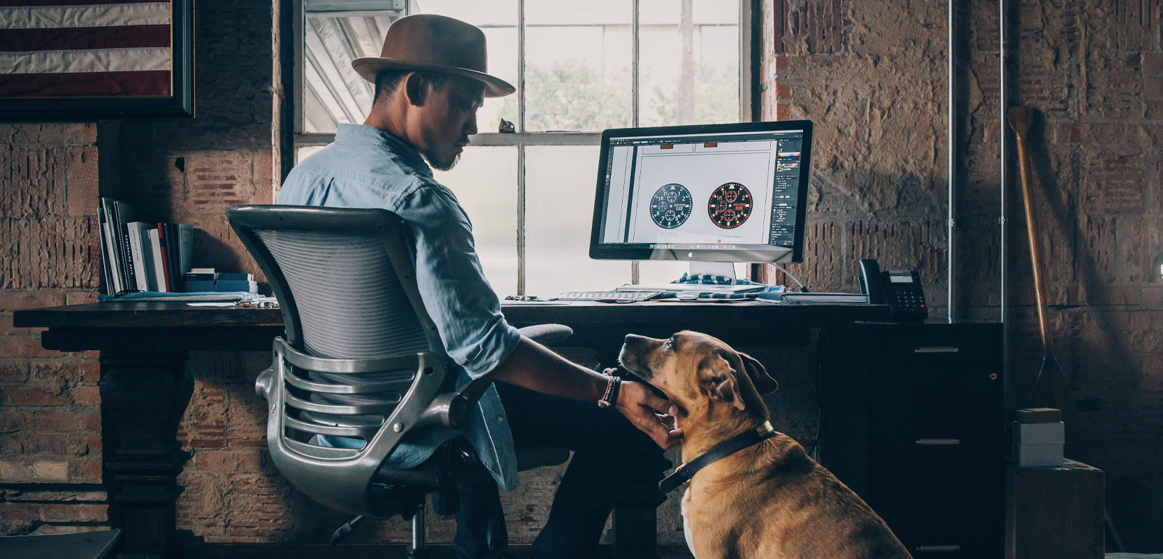 Professional pet sitter at a desk in front of a computer, petting a brown dog and preparing to set up a pet sitting LLC