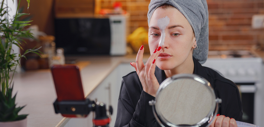 A woman testing out a clay face mask in front of a mirror