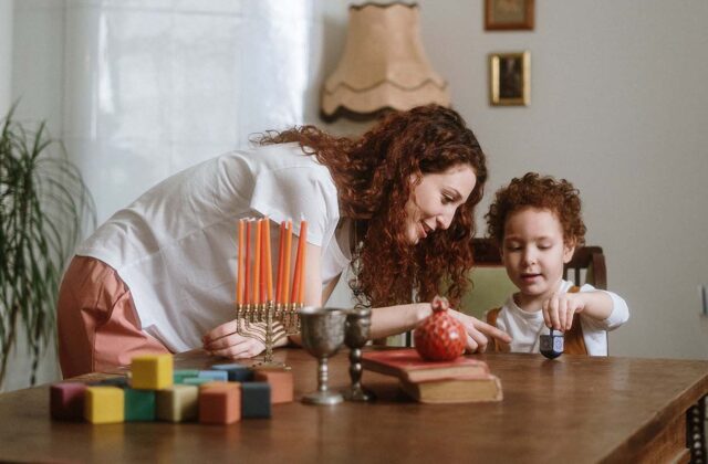 App-based babysitter watching after a young child playing with a dreidel at home