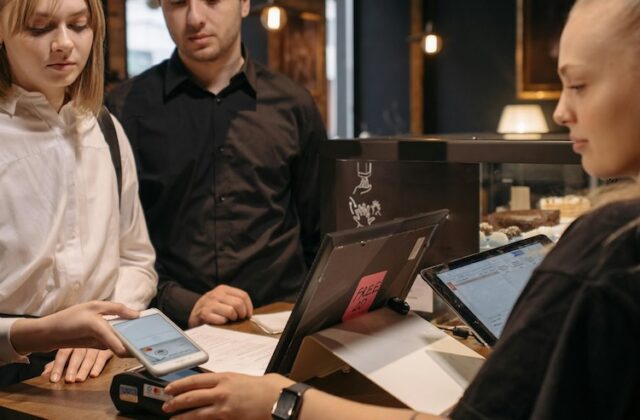 A woman making a contactless payment at a counter using a mobile phone.