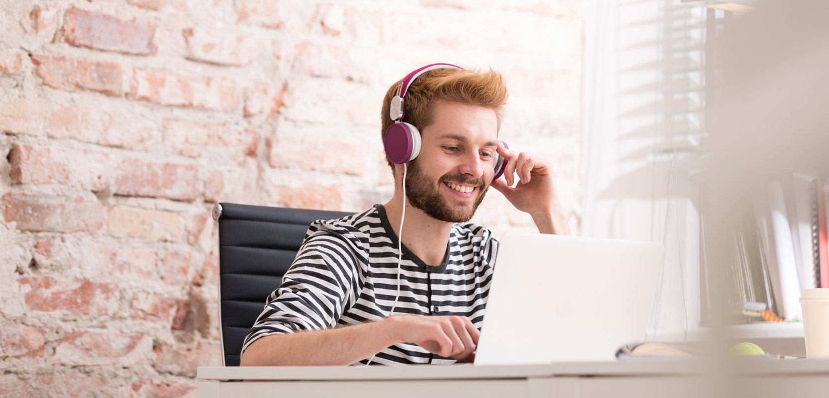 Man sitting at his desk at home wearing headphones and transcribing an article on his laptop