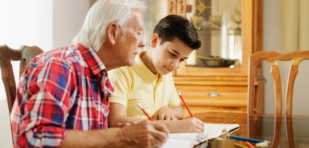 Older man sitting next to a child and tutoring him in a school subject