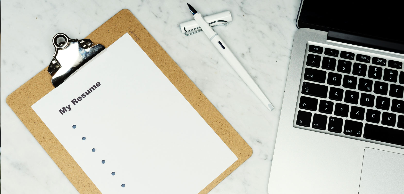 Clipboard with an unfinished resume on a table next to a laptop