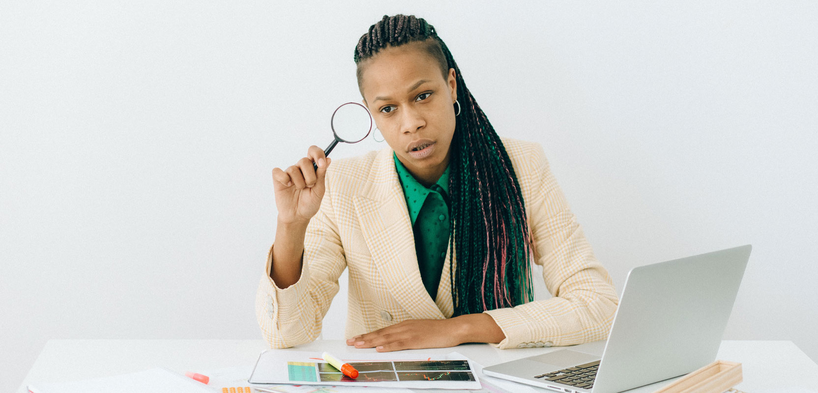 Woman sitting in front of a laptop and looking through a magnifying glass