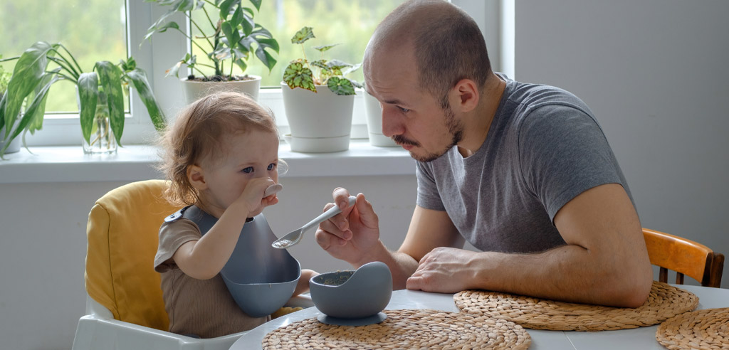 Babysitter feeding a small child at a table
