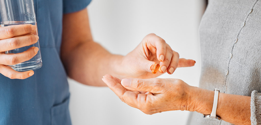 Caregiver handing their care receiver a pill and a glass of water