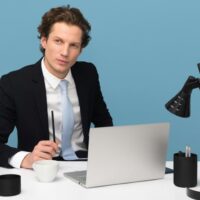 Professional consultant in a suit looking thoughtful and sitting at a white desk with a laptop and mug