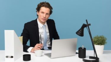 Professional consultant in a suit looking thoughtful and sitting at a white desk with a laptop and mug