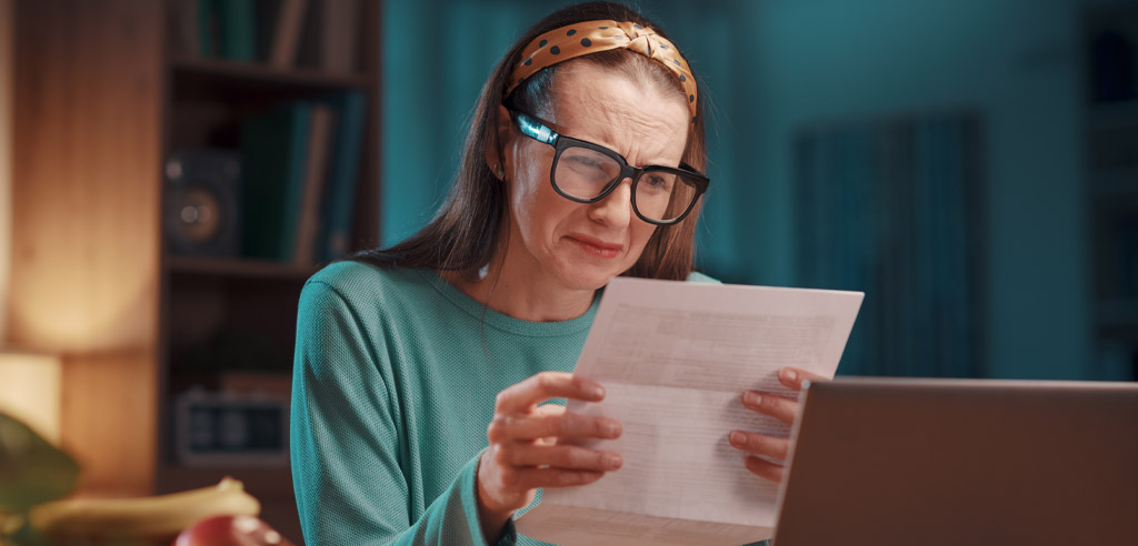 Older woman sitting in her home and squinting at an expensive bill with a worried expression