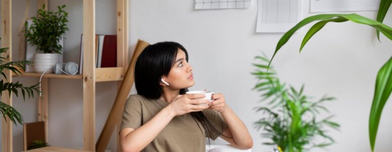 Woman at desk drinking coffee and looking at a wall calendar.