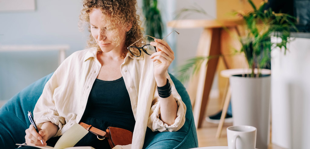 Writer sitting in a comfortable chair at home and writing in a notebook for her side hustle